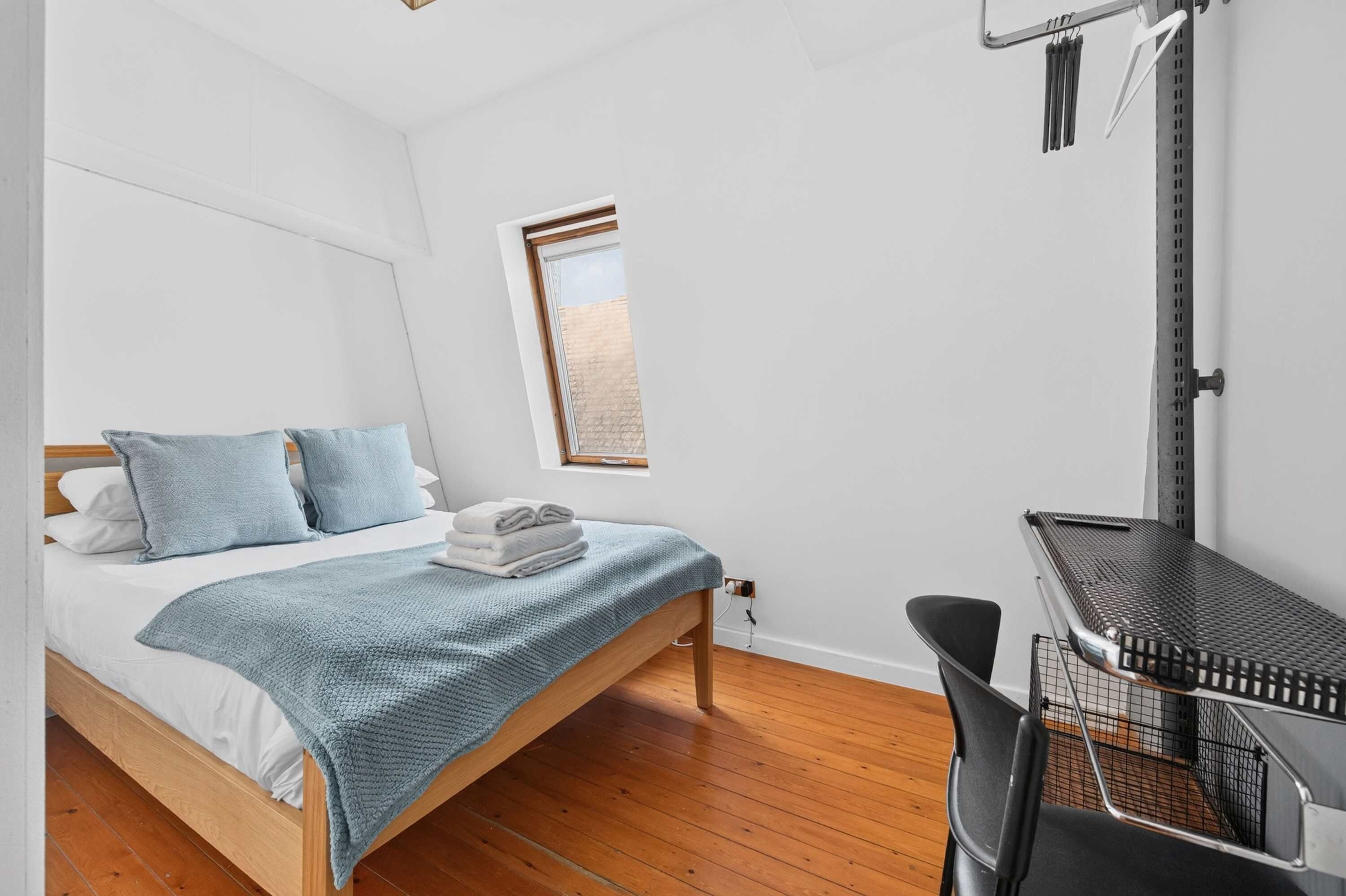 Une chambre à coucher avec un lit, une petite fenêtre, un bureau et une chaise.