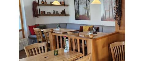 Un restaurante acogedor con mesas y sillas de madera, iluminación colgante y obras de arte en las paredes.