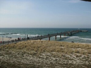 A coastal scene with a pier extending into the sea, sandy beach, and grassy dunes. - 13b/t4 Holiday Home Park \"freesenbruch\" (Zingst)