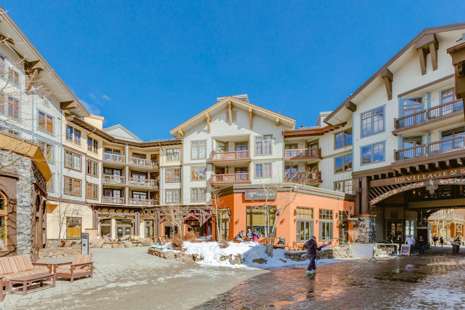 Un hotel de varios pisos con balcones, un patio central nevado y mesas al aire libre.