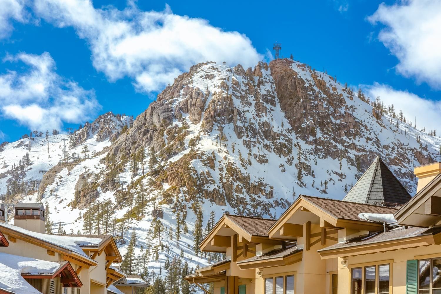 A mountain with a cross on top, surrounded by snow-covered peaks and pine trees.