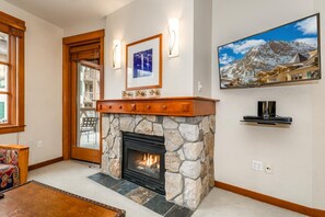 A room with a stone fireplace, a mounted television, and a framed picture on the wall. - Palisades Ski Resort Condo | Steps to Gondola (Tahoe City)