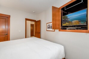 A hotel room with a bed, a television mounted on the wall, and a door leading to another room. - Palisades Ski Resort Condo | Steps to Gondola (Tahoe City)