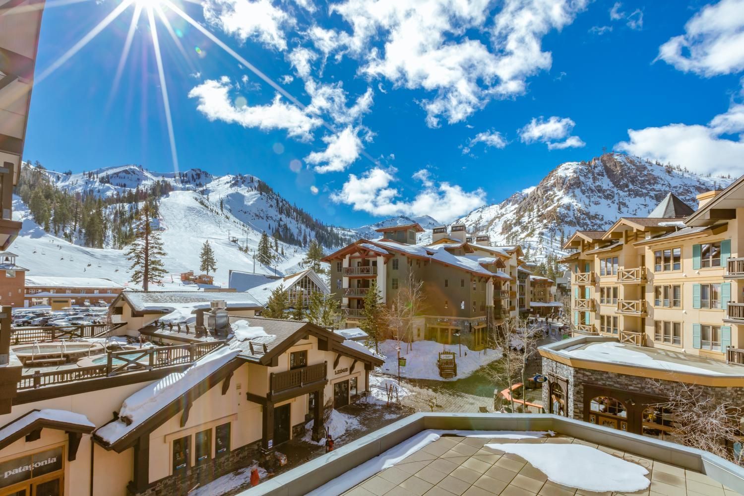 A snow-covered mountain resort with multiple buildings, including a hotel with balconies and a pool area.