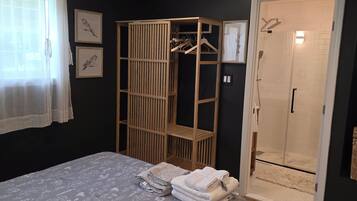 A bedroom with a bed, a wooden wardrobe, a shower, and a window with curtains.