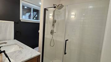 A bathroom with a glass-enclosed shower, a marble sink, and a wooden vanity.