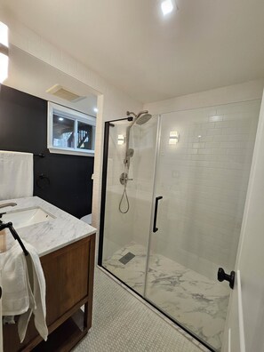 A bathroom with a glass-enclosed shower, a marble sink, and a wooden vanity.