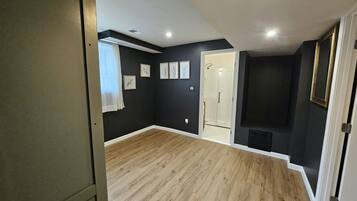 A room with a wooden floor, a door, a window with curtains, and a wall with framed pictures.