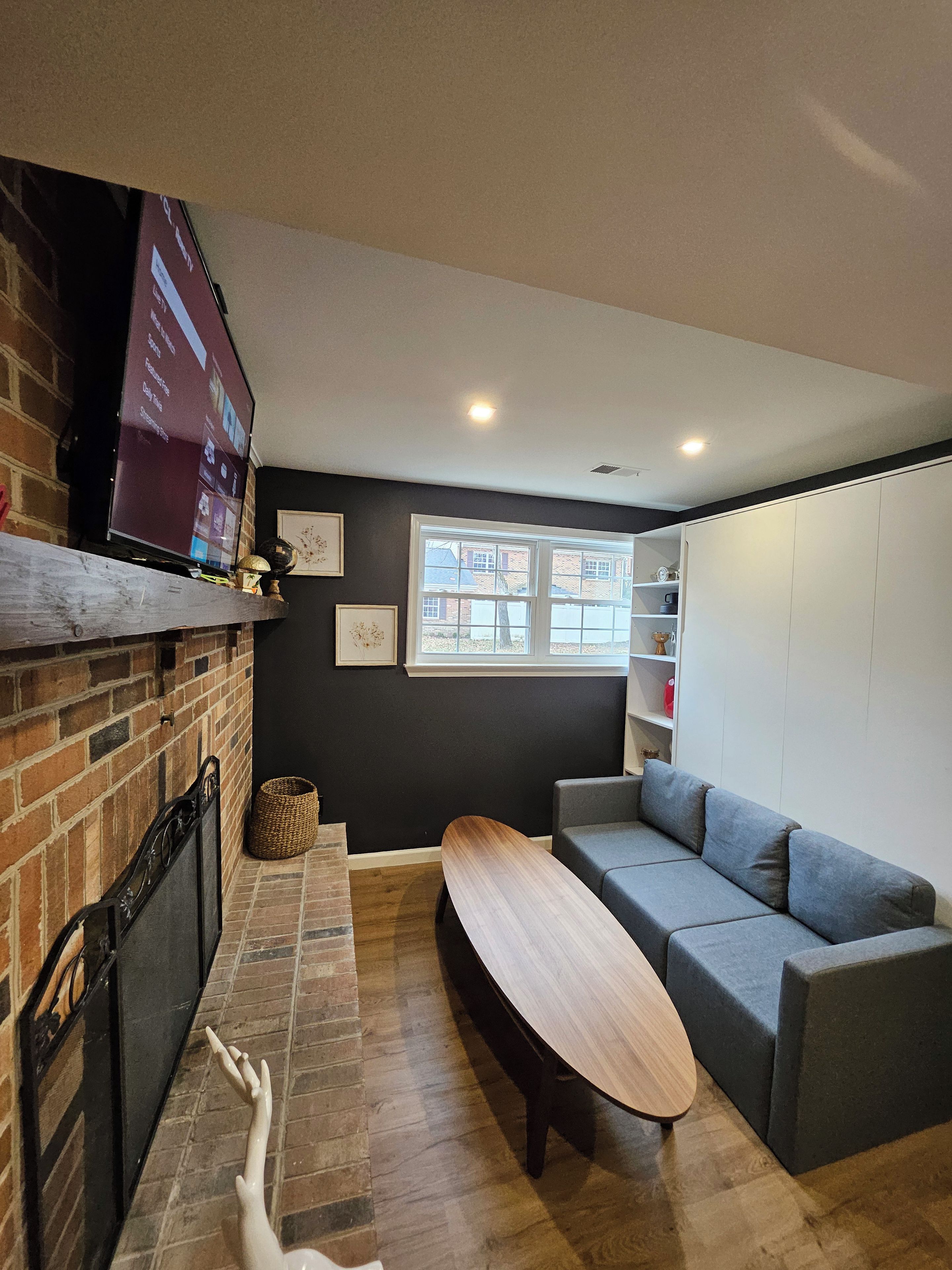 Ein modernes Wohnzimmer mit Kamin, Flachbildfernseher, grauem Sofa und Holztisch.