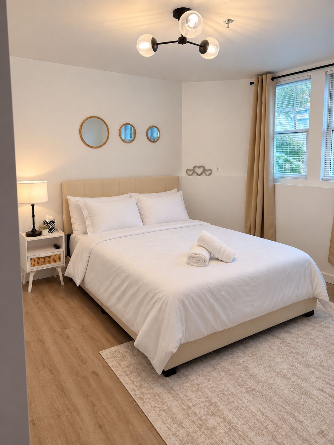 A neatly made bed with white linens, a bedside lamp, and a small nightstand with a plant.