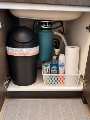 A bathroom with a toilet, a trash can, a water heater, and a storage basket containing cleaning supplies. - Midtown Gem Near Downtown (Detroit)