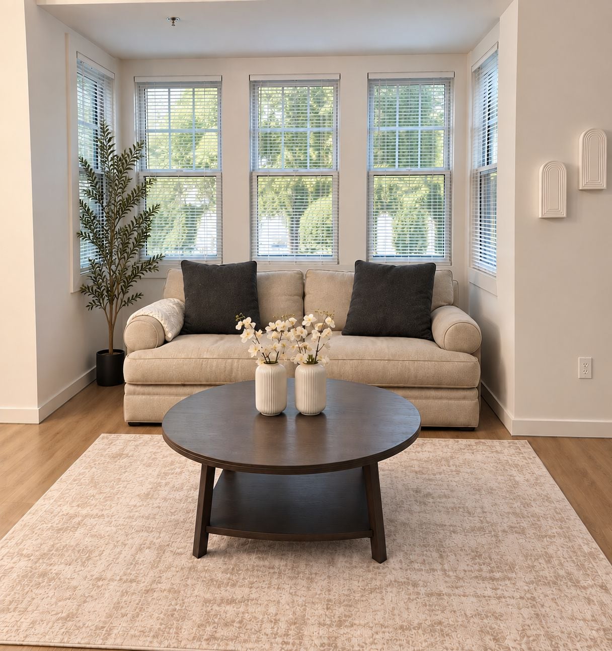 A living room with a beige sofa, two vases with white flowers, a dark coffee table, and a potted plant.