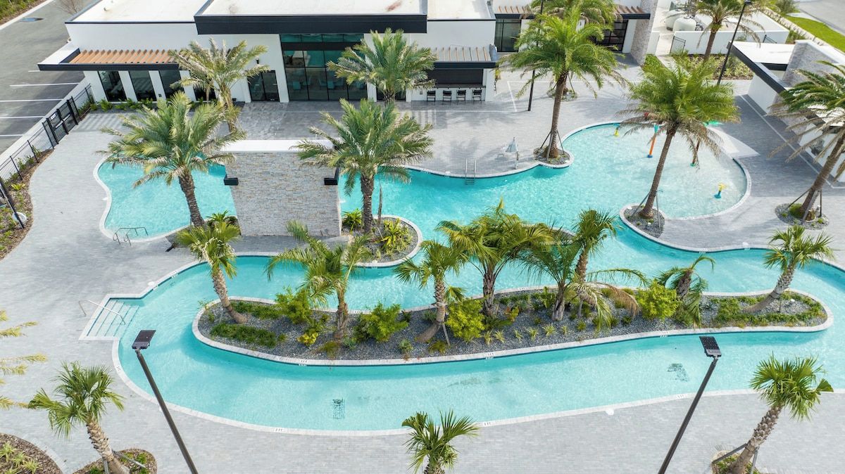 A modern hotel with a central swimming pool surrounded by palm trees and a paved walkway.