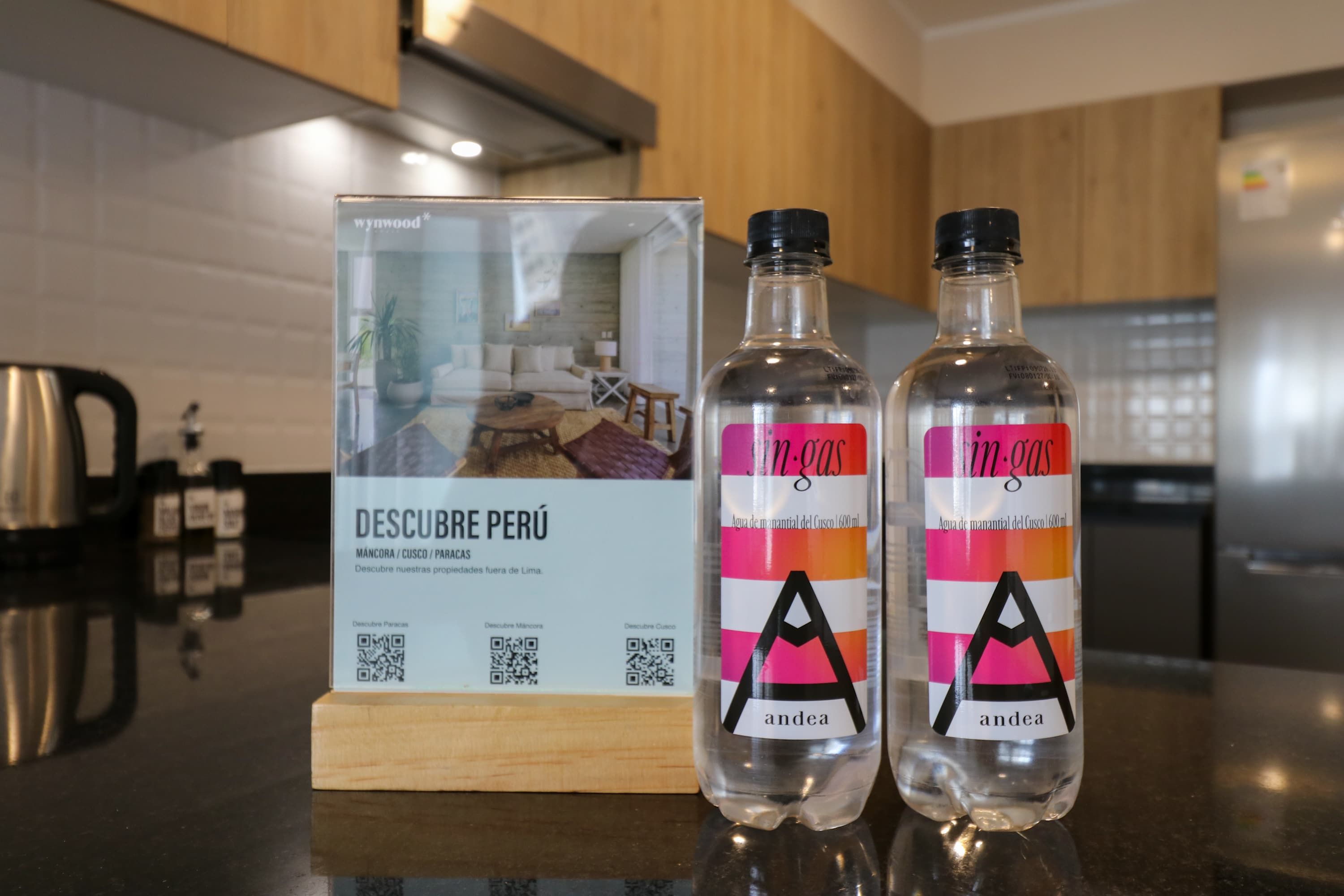 Two bottles of 'in gas' water on a kitchen counter with a QR code and a sign about 'DESCUBE PERÚ'.