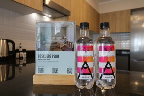 Dos botellas de agua 'in gas' sobre una encimera de cocina, con un código QR y un cartel que dice 'DESCUBE PERÚ'.