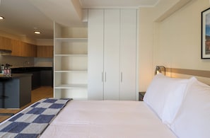 A hotel room with a bed, a nightstand, a lamp, a wardrobe, and a kitchen area. - w* | Charming Loft w/ Balcony in Prime Miraflores (Miraflores)