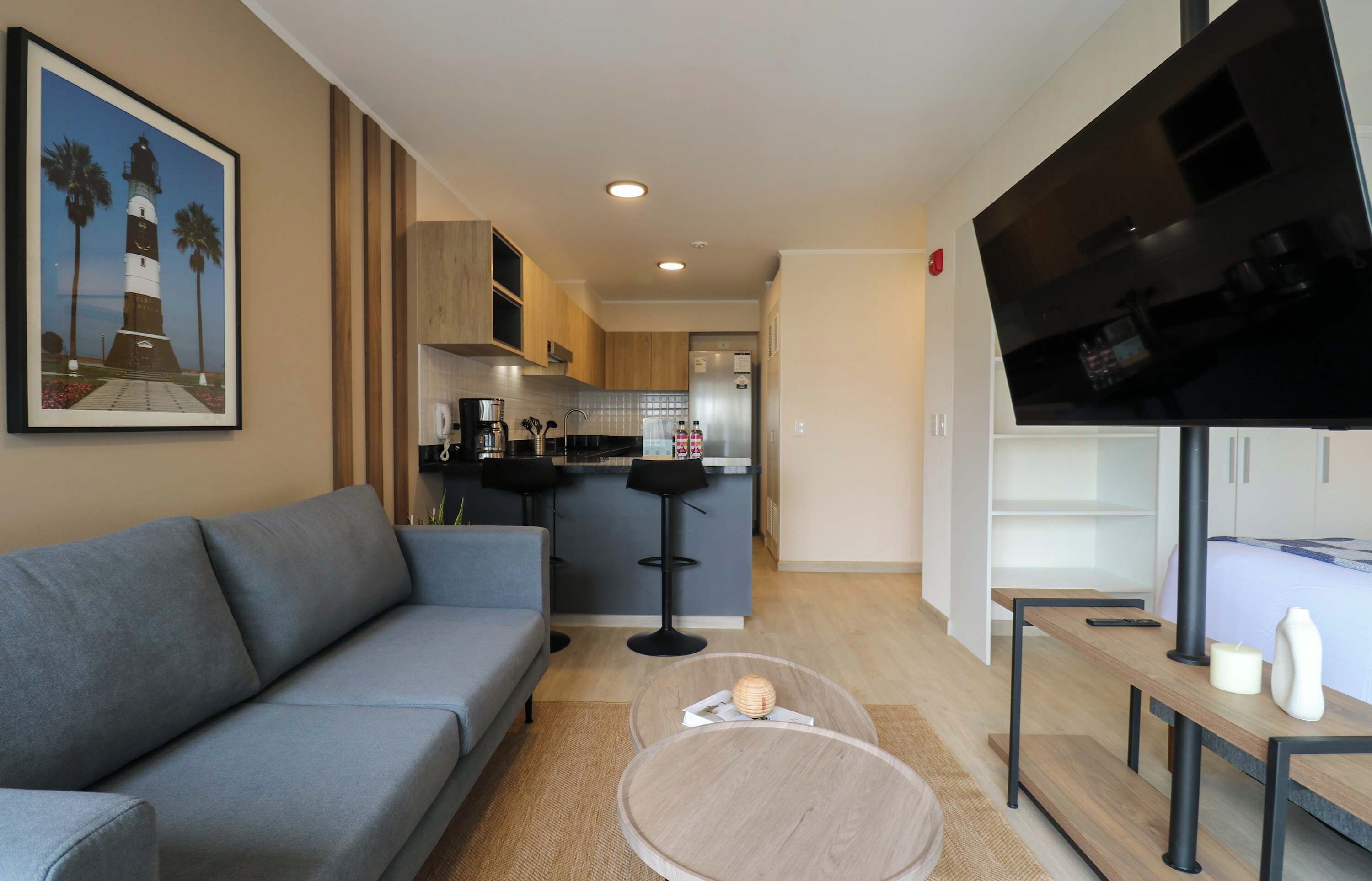 A modern living room with a grey sofa, a coffee table, a TV, and a kitchen in the background.