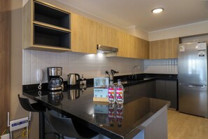 A modern kitchen with wooden cabinets, a stainless steel refrigerator, a coffee maker, and two bottles of water. - w* | Charming Loft w/ Balcony in Prime Miraflores (Miraflores)