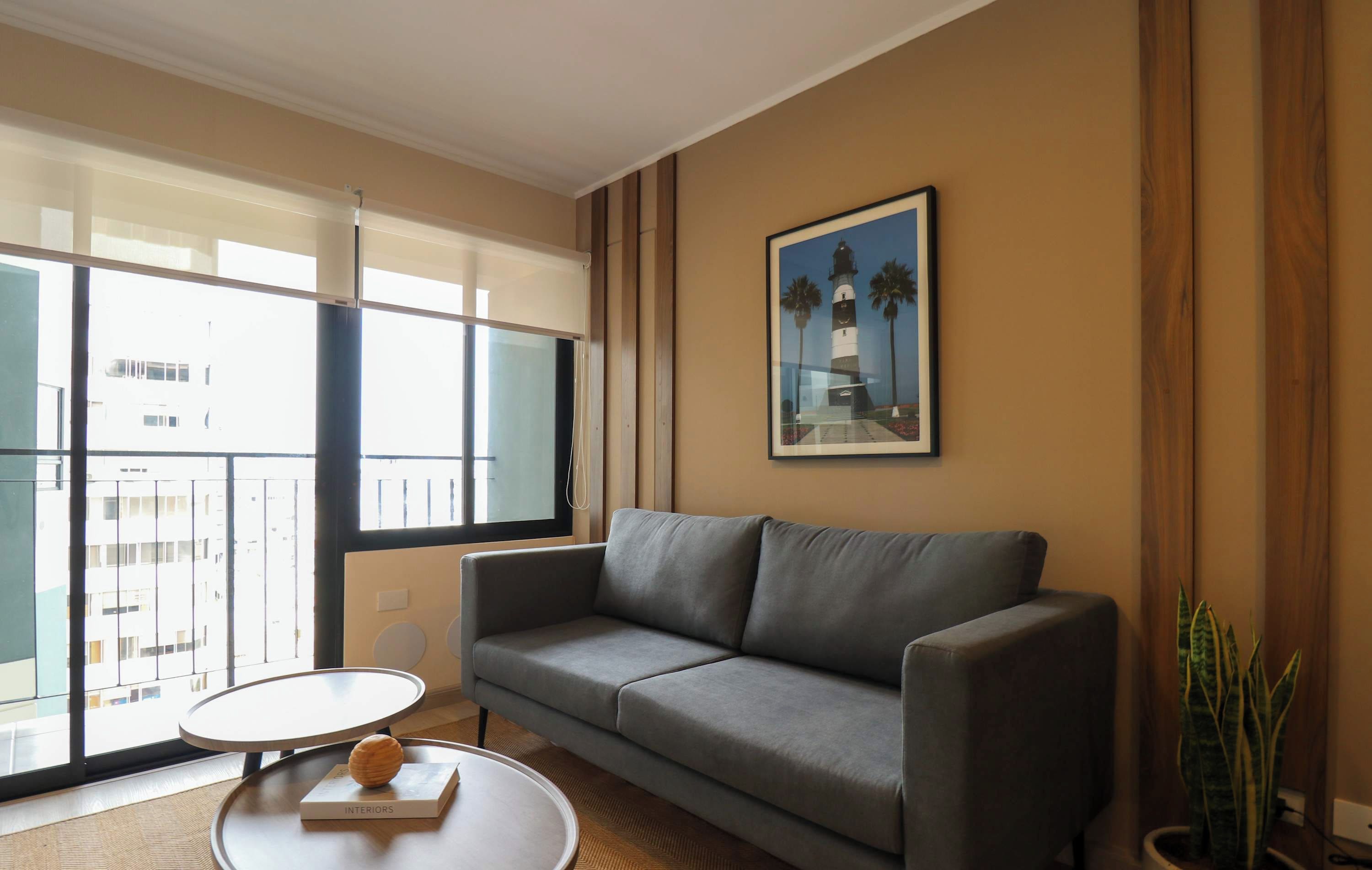 Un salon moderne avec un canapé gris, une table basse ronde et un tableau encadré représentant un phare, accroché au mur.