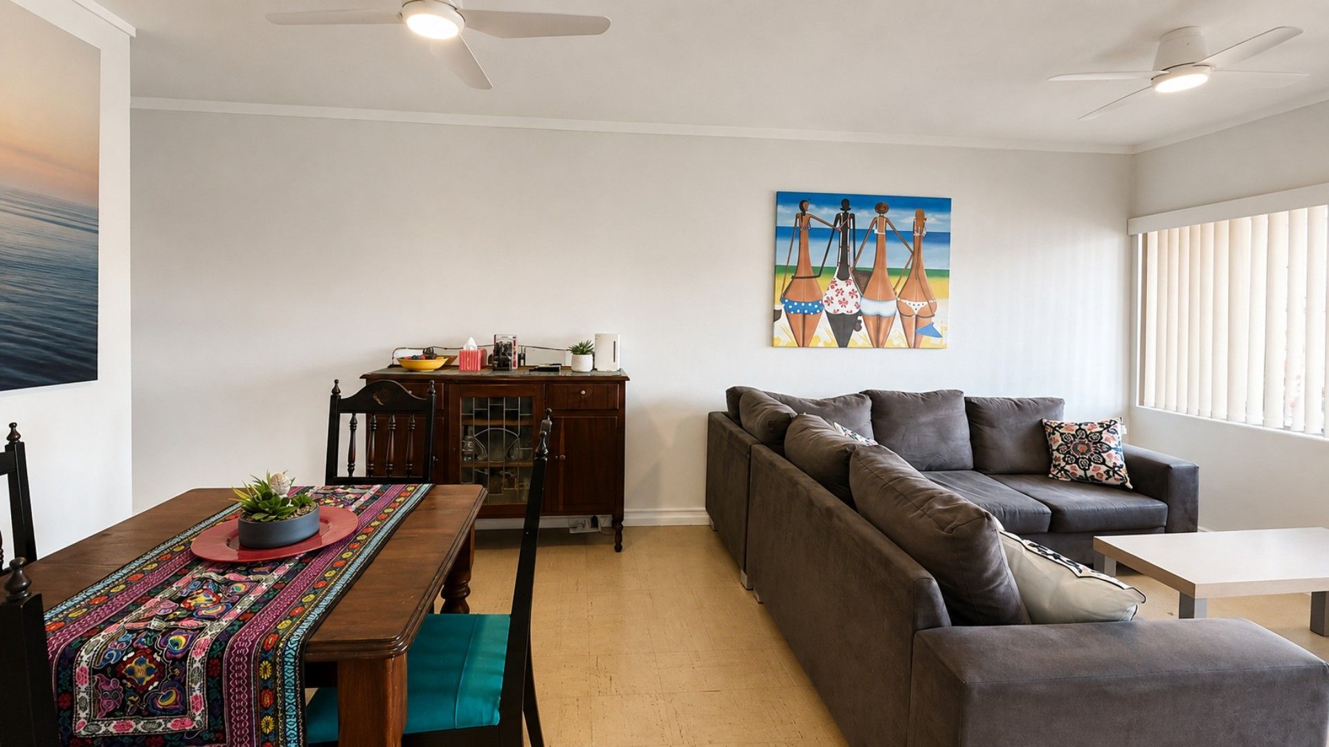 A living room with a sofa, a dining table with chairs, and a ceiling fan.