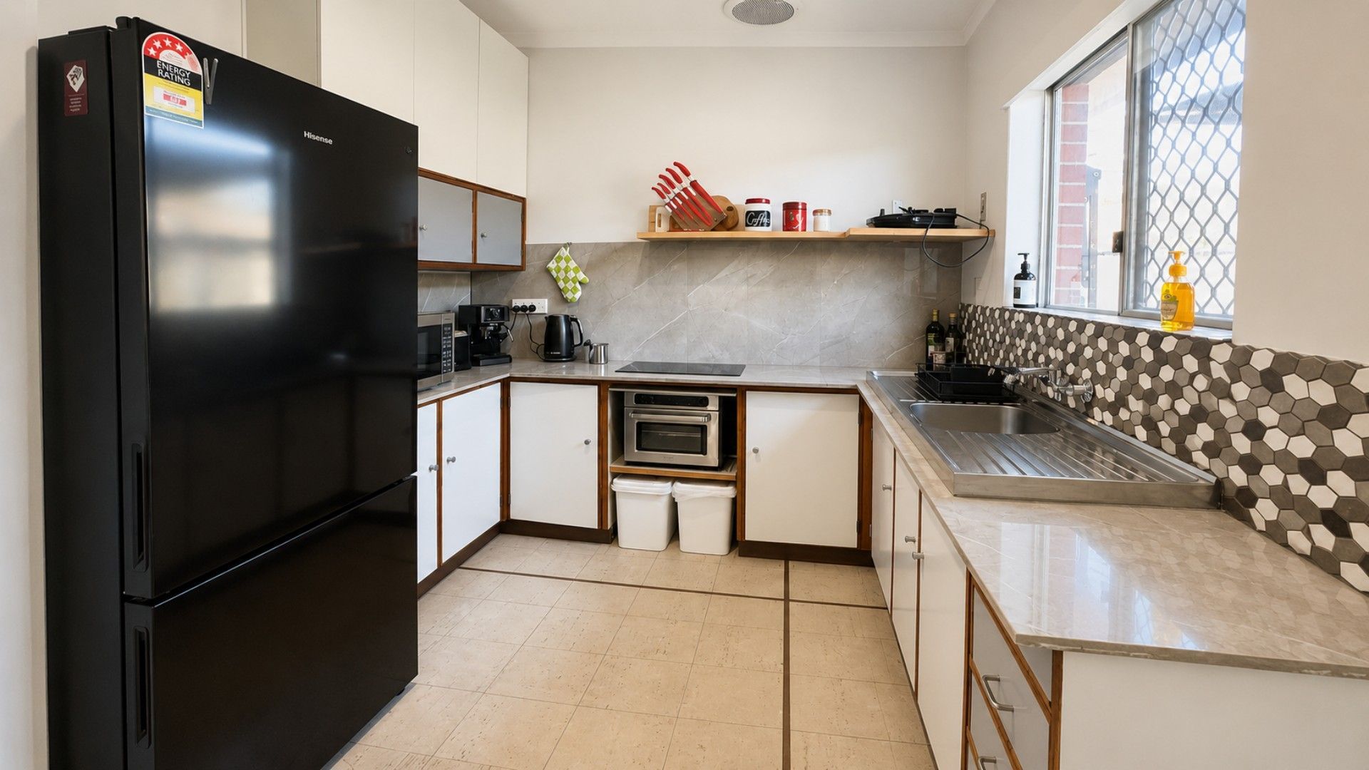 A compact kitchen with a black refrigerator, a built-in oven, a coffee maker, and a window with a view.