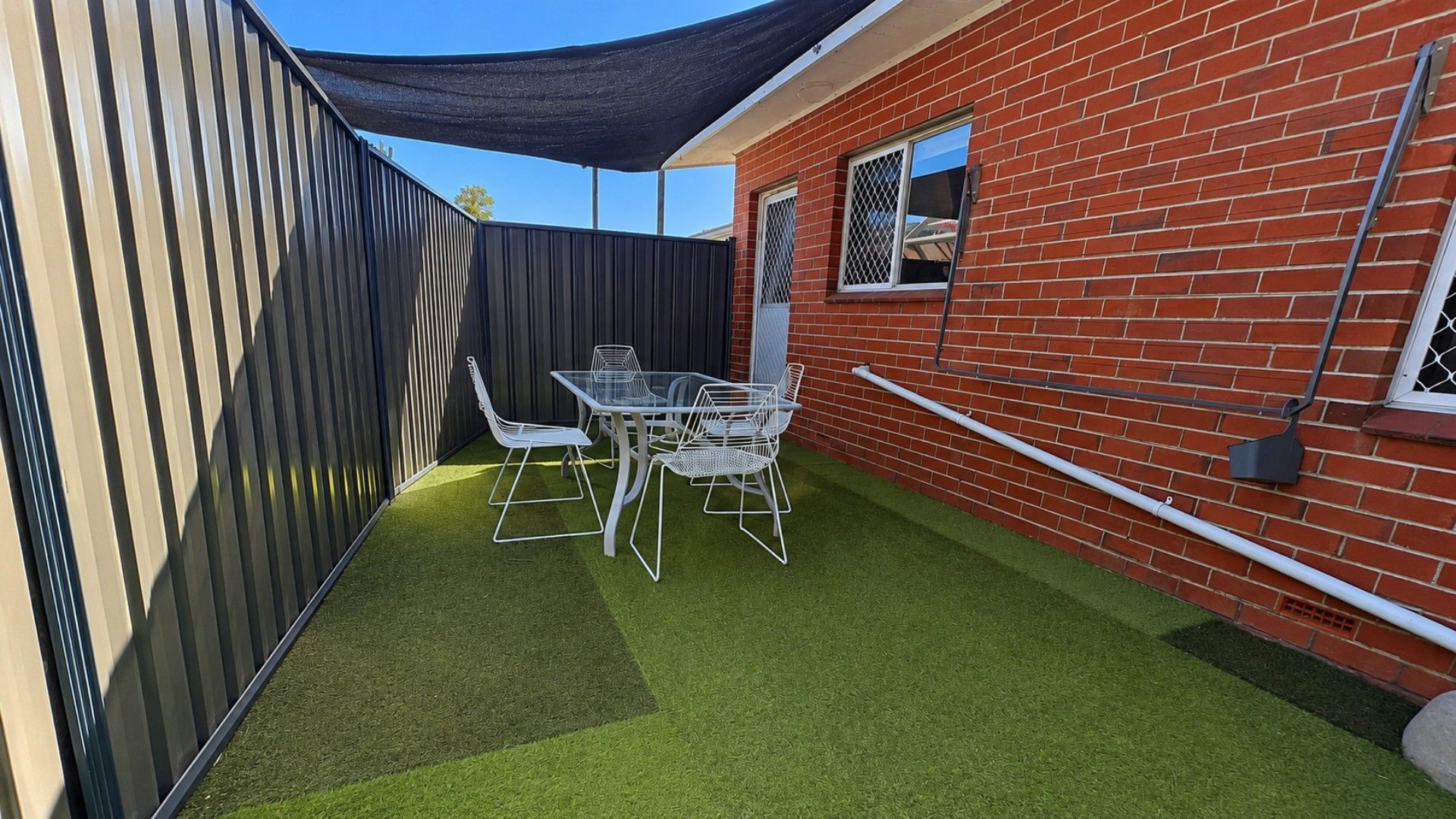 A patio with a table and chairs, a brick wall, and a metal fence.