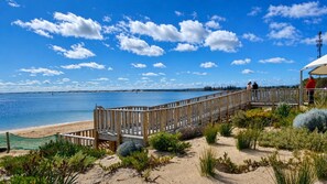 A wooden boardwalk leading to a beach with a clear view of the water and a distant shoreline.