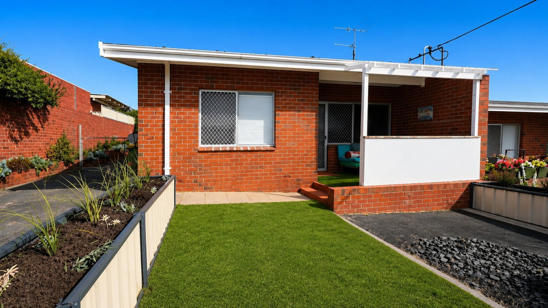 A residential house with a brick exterior, a front porch, a small front yard with artificial grass, and a visible satellite dish.