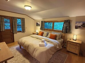 Une chambre à coucher avec un lit, des tables de chevet, une commode, une fenêtre avec des rideaux et une porte.