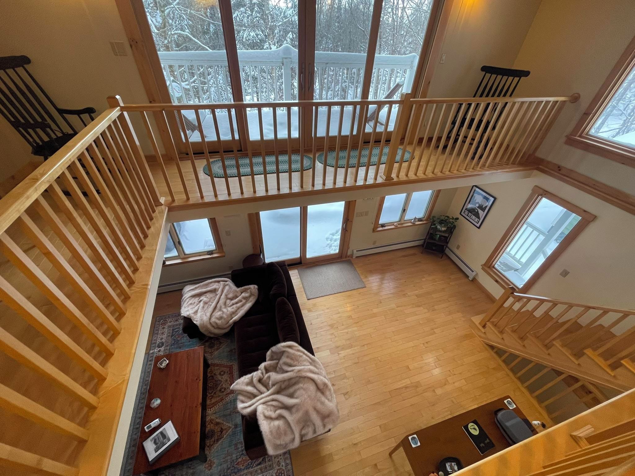 A spacious loft with a high ceiling, a wooden staircase, a cozy seating area with a sofa and chairs, and large windows offering a view of a snowy landscape.