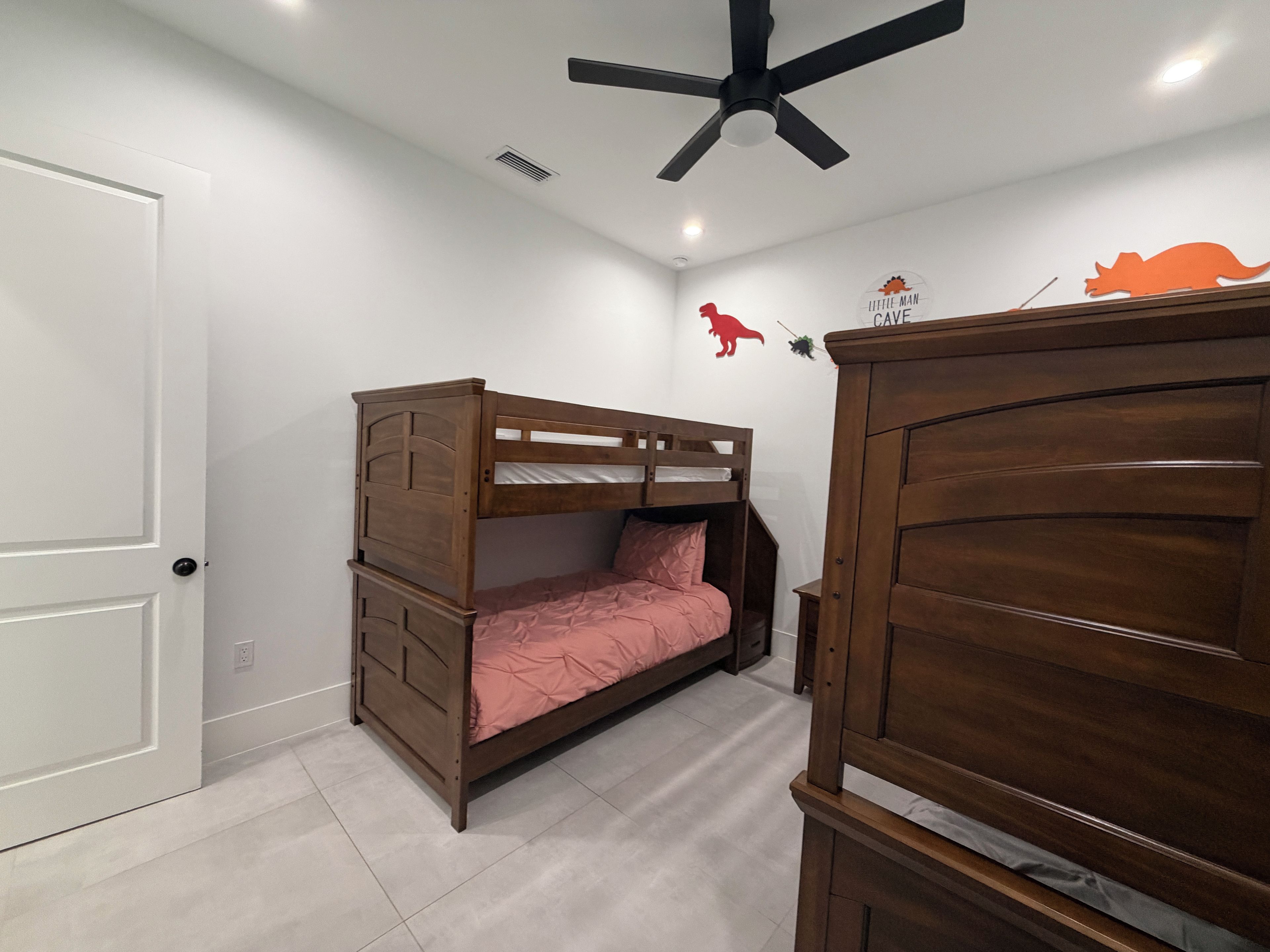 A room with a bunk bed, a ceiling fan, a wall decal, and a door.