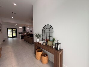 A modern living space with a central console, a large mirror, and a view into the kitchen area.