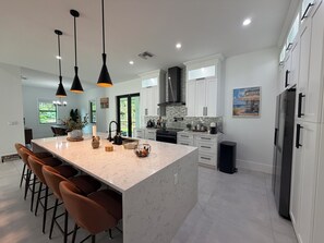 A modern kitchen with a central island, bar stools, pendant lighting, and a view of the outdoors.