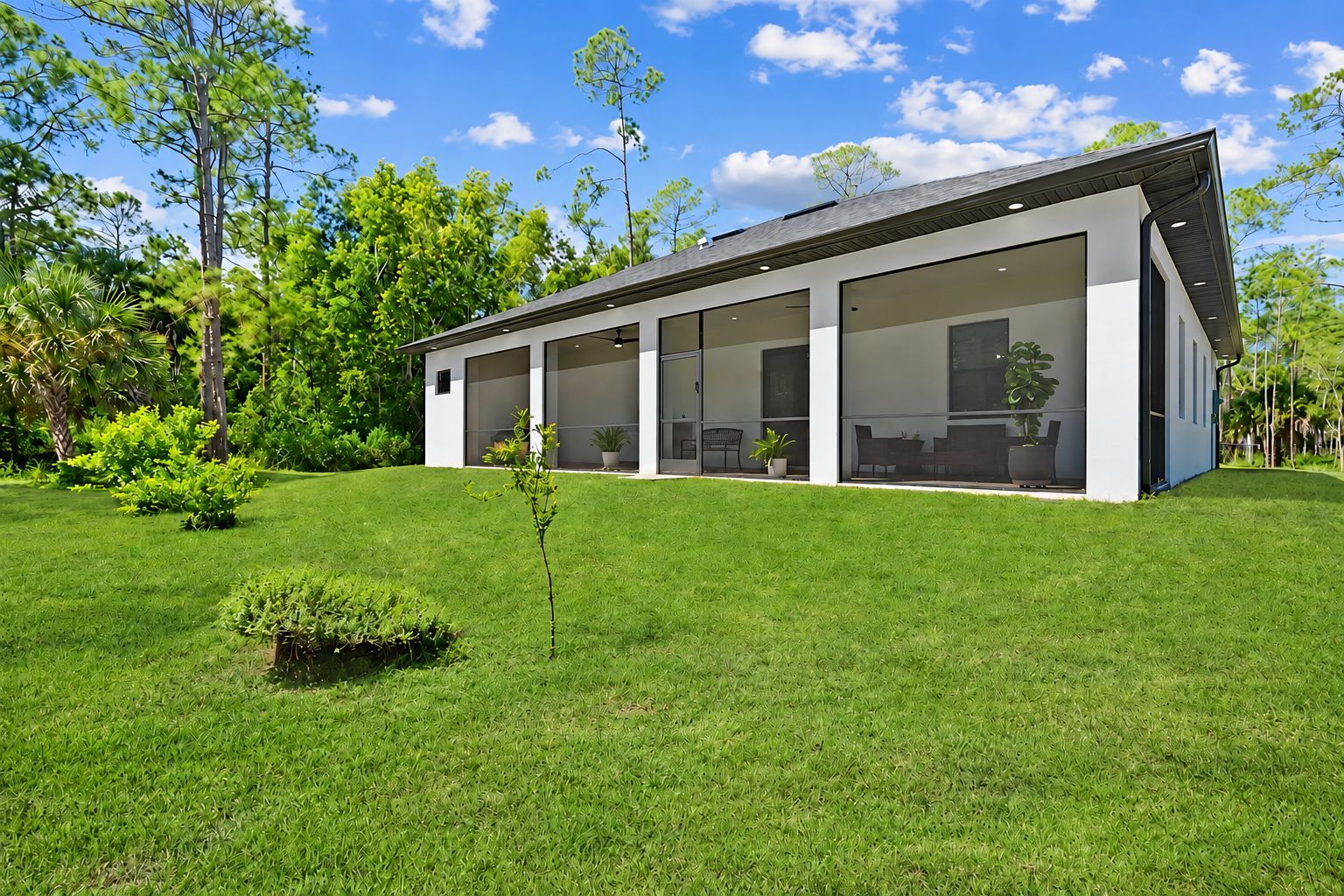 Una casa moderna con un amplio ventanal, rodeada de un césped cuidado y árboles.