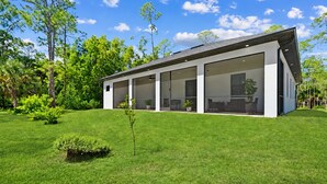 A modern house with a large glass facade, surrounded by a well-maintained lawn and trees.
