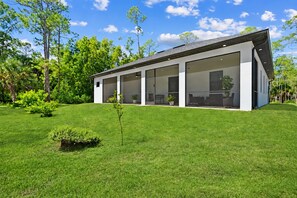 Una casa moderna con un amplio ventanal, rodeada de un césped cuidado y árboles.