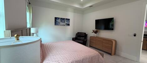 A bedroom with a bed, a desk, a chair, a television, and a ceiling fan.
