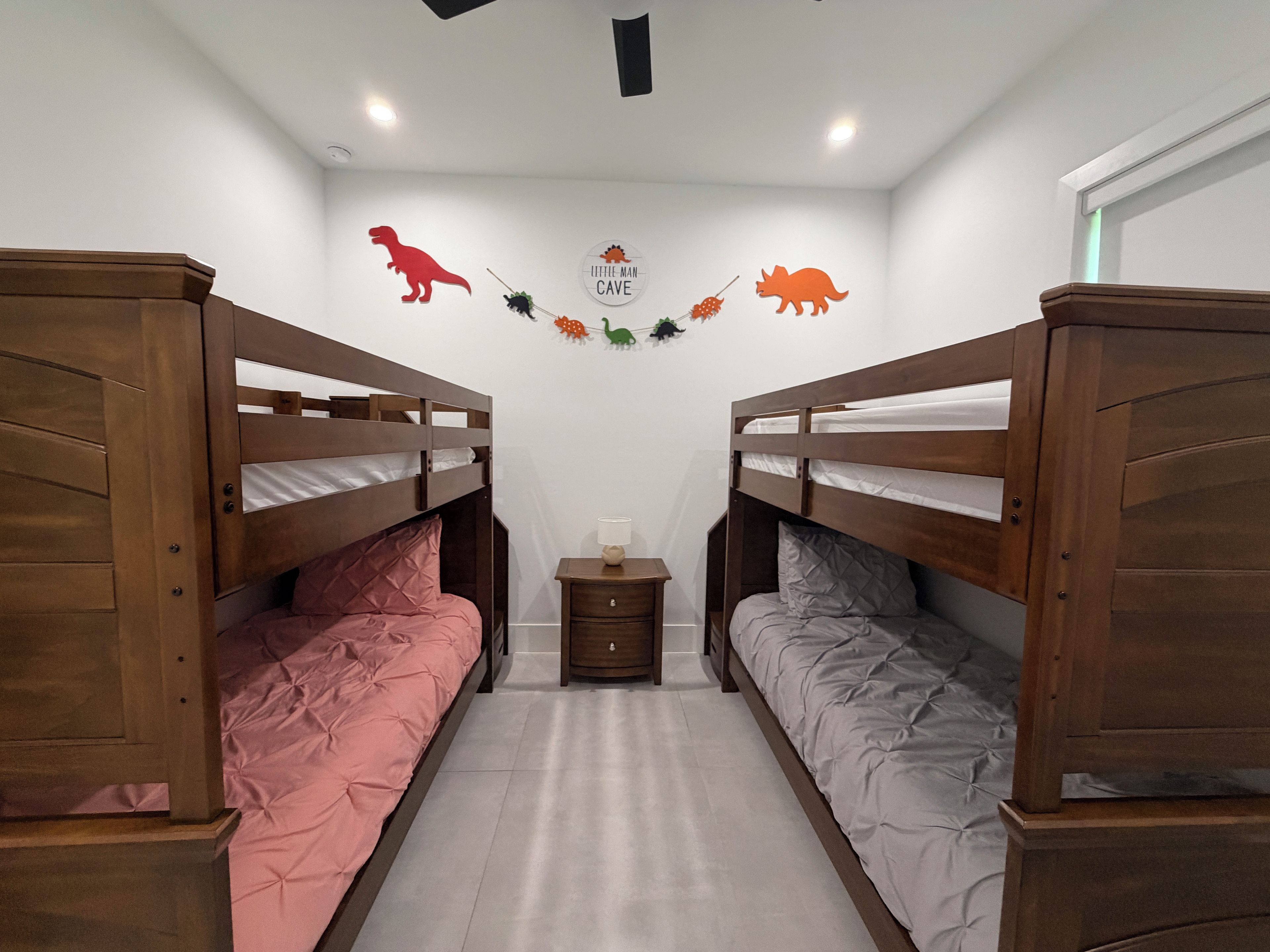 Ein Zimmer mit zwei Etagenbetten, einem kleinen Nachttisch mit Lampe sowie Wanddekorationen, darunter Dinosaurierfiguren und ein Schild mit der Aufschrift 'Little Man Cave'.