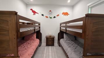 Ein Zimmer mit zwei Etagenbetten, einem kleinen Nachttisch mit Lampe sowie Wanddekorationen, darunter Dinosaurierfiguren und ein Schild mit der Aufschrift 'Little Man Cave'.