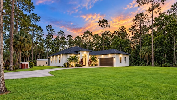 A single-story house with a dark roof, surrounded by a well-maintained lawn and tall trees.