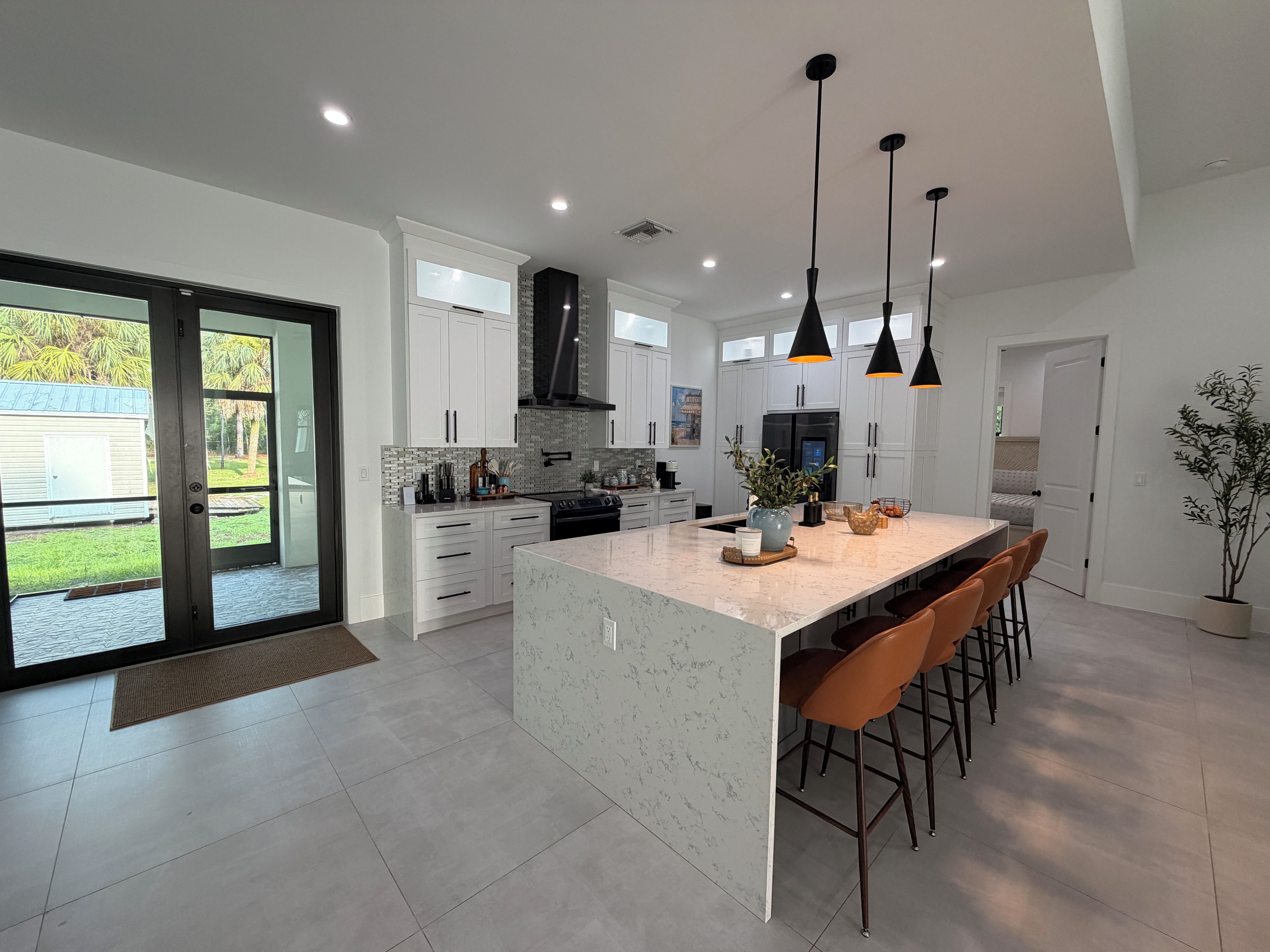 A modern kitchen with white cabinetry, a marble island, and pendant lighting.