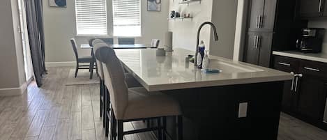 A modern kitchen with a central island, bar stools, and a dining area with a bench.