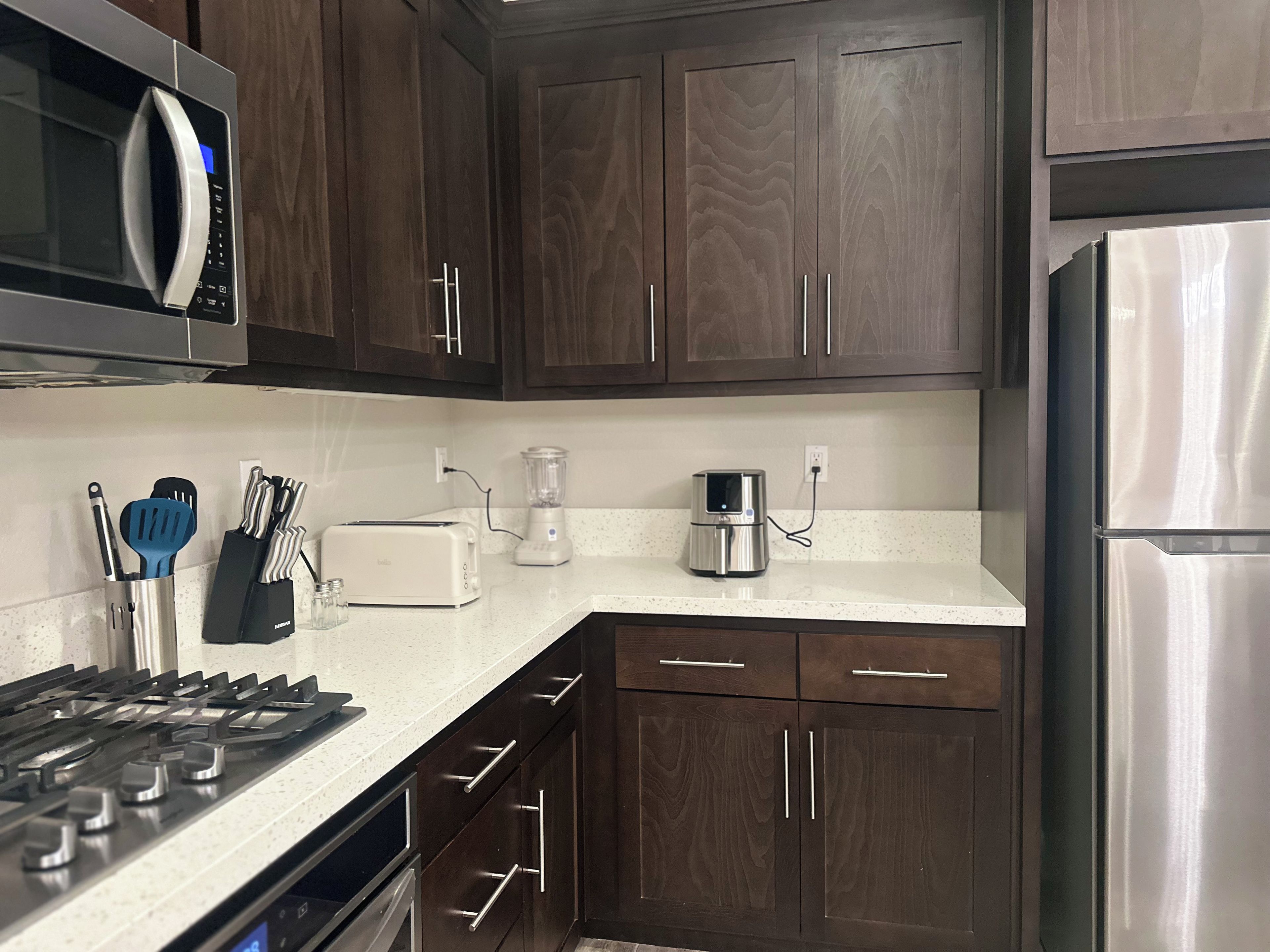 A kitchen with dark wood cabinets, a stainless steel refrigerator, a microwave, a toaster, and a blender.