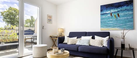 A modern living room with a dark blue sofa, a round wooden coffee table, and a large abstract painting on the wall.