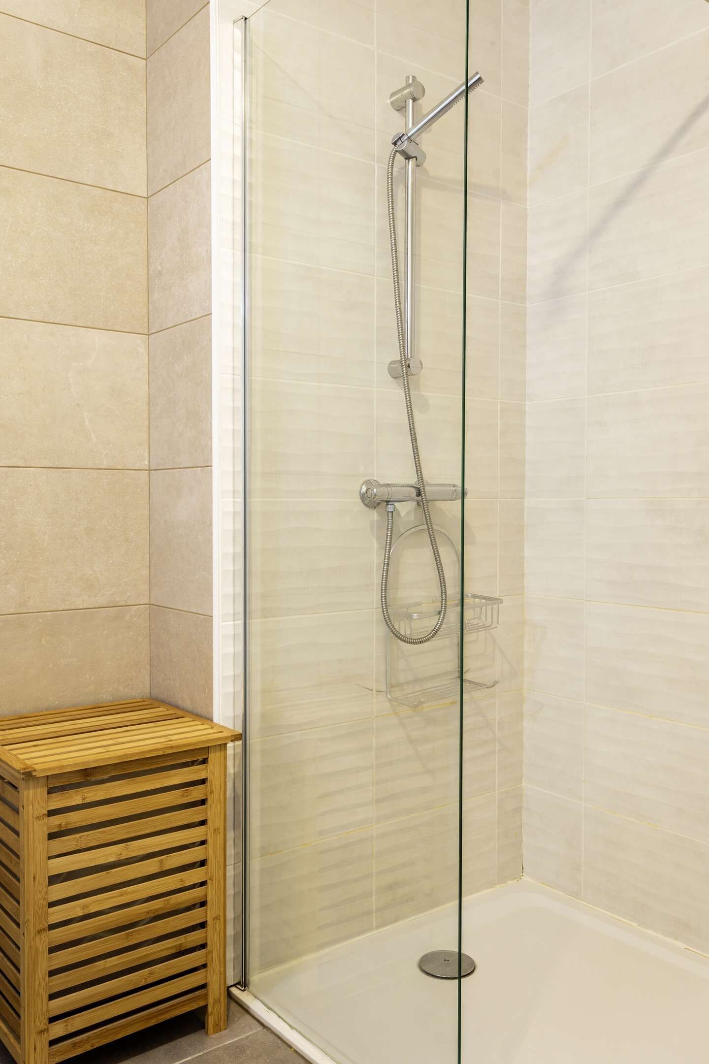 A glass-enclosed shower stall with a handheld showerhead and a wall-mounted faucet.