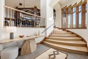 A modern staircase with wooden steps and a metal railing, leading to a second-floor area with a dining setup. - Northside Retreat| Ski-In/Out | Hot Tub (Park City)