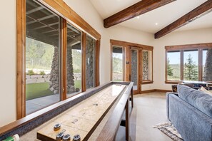 A room with a shuffleboard table, large windows, a stone wall, and a sofa. - Northside Retreat| Ski-In/Out | Hot Tub (Park City)