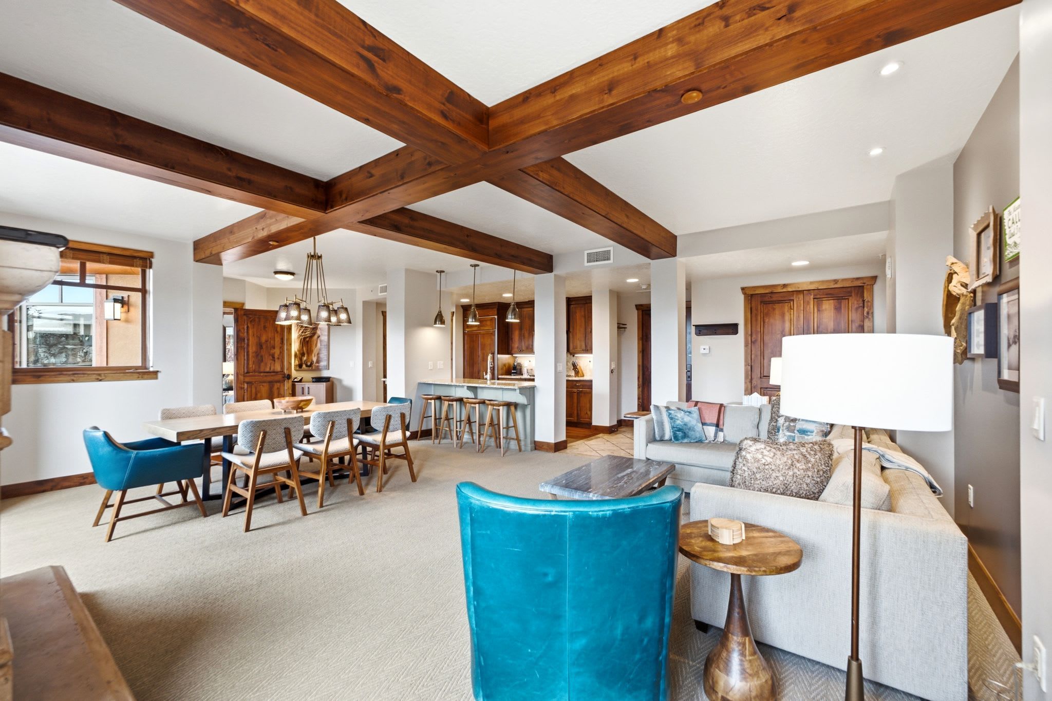 A spacious living area with a high ceiling and exposed wooden beams, a dining area with a large table and chairs, and a kitchen with wooden cabinets.