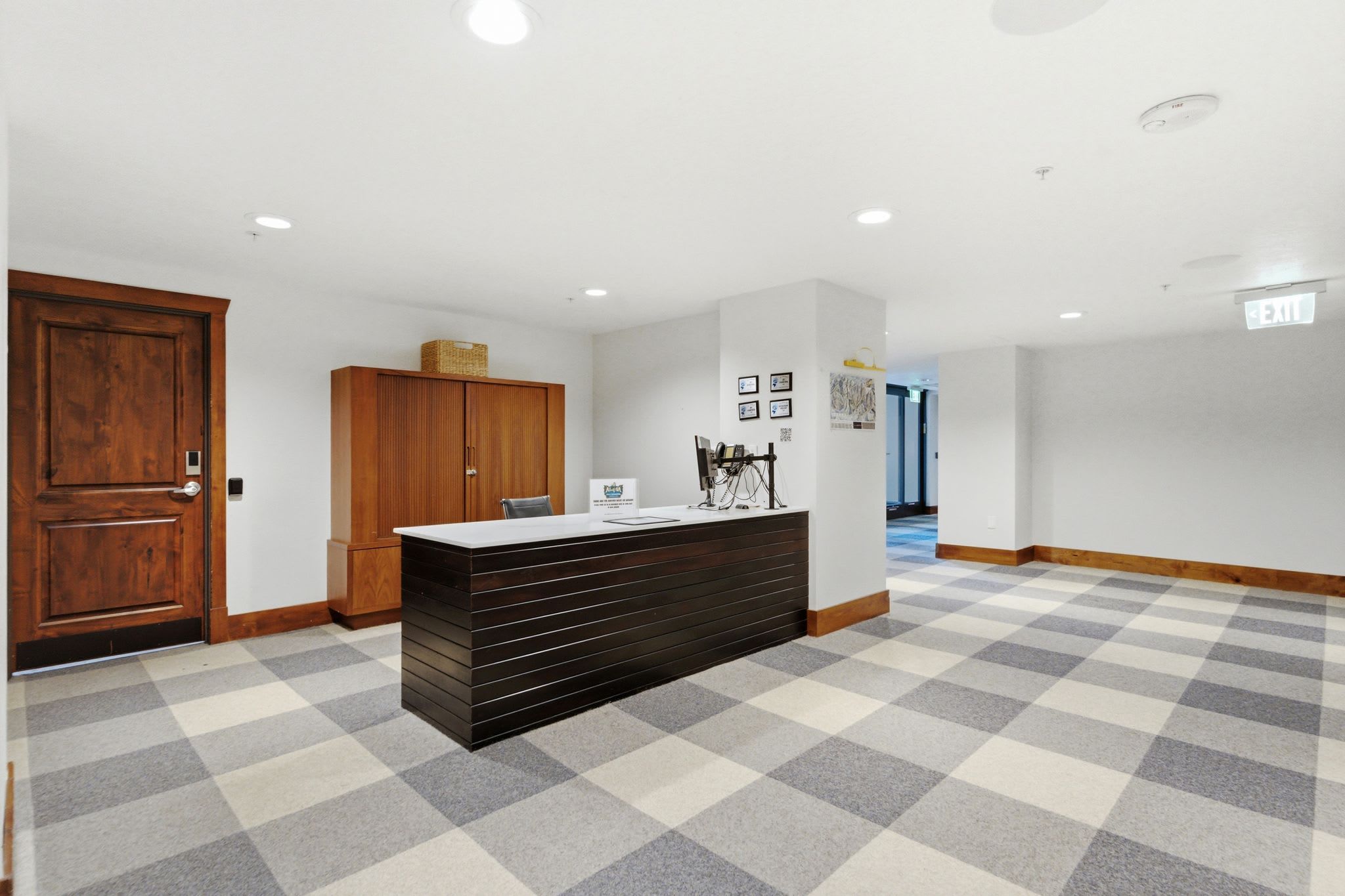 A reception area with a checkered floor, a wooden door, a reception desk, and a wall with framed pictures.