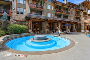 A multi-story building with a pool area featuring lounge chairs and a hot tub. - Ski-in/Ski-out | Heated Pool, Hot Tubs & Game Room | Shuttle To Main St. (Park City)
